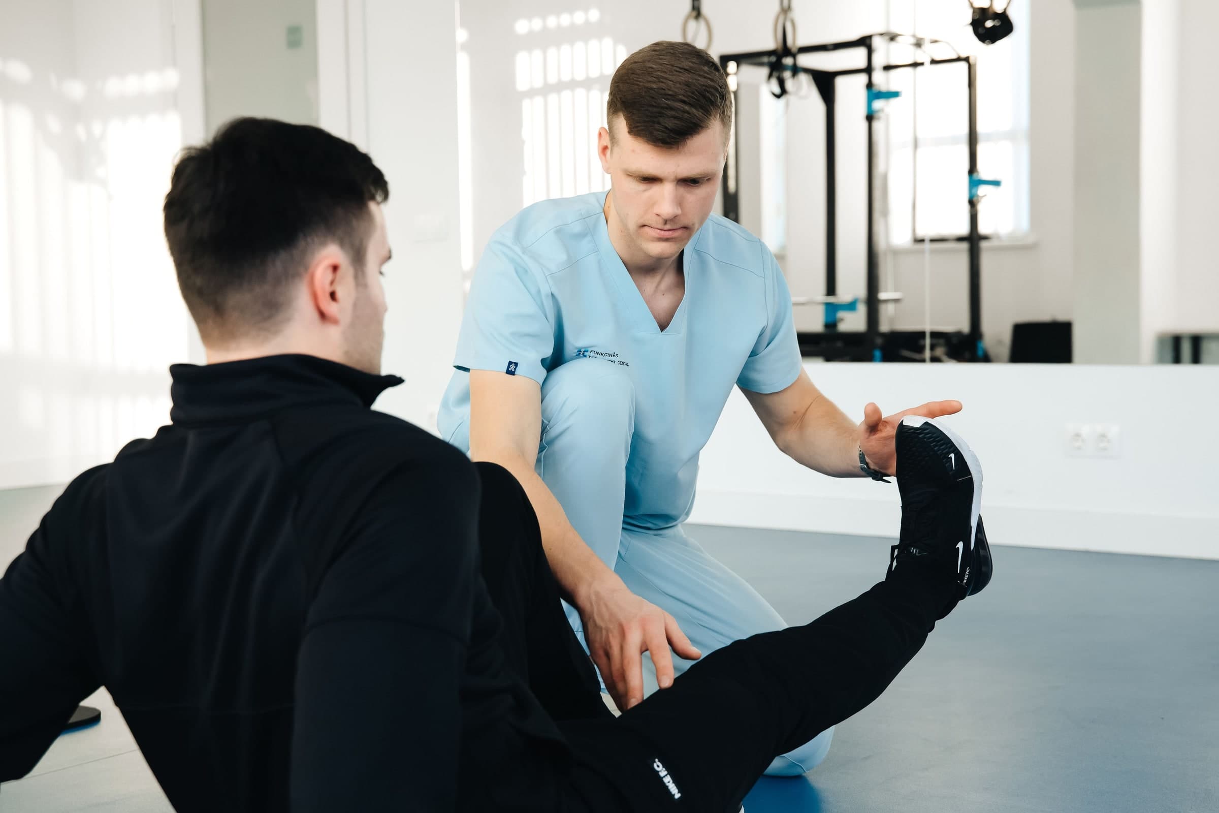 Physiotherapist in light blue scrubs examining a patient's ankle and foot during a treatment session in a bright clinical room in Toronto