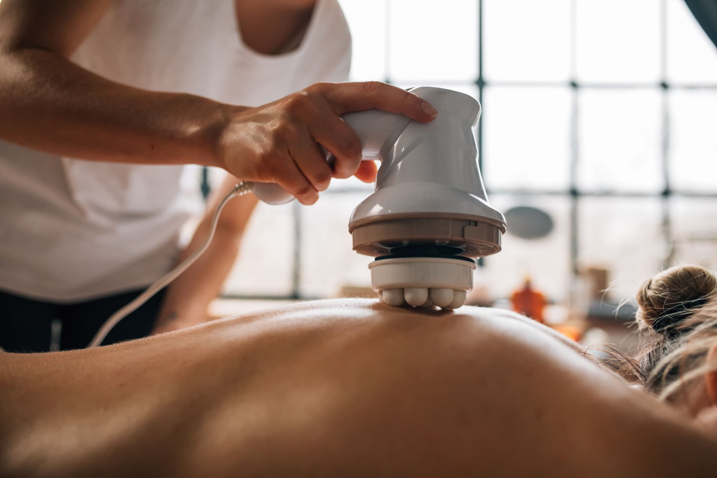 A practitioner using a handheld percussion massage device on a patient's back during a treatment session in Toronto