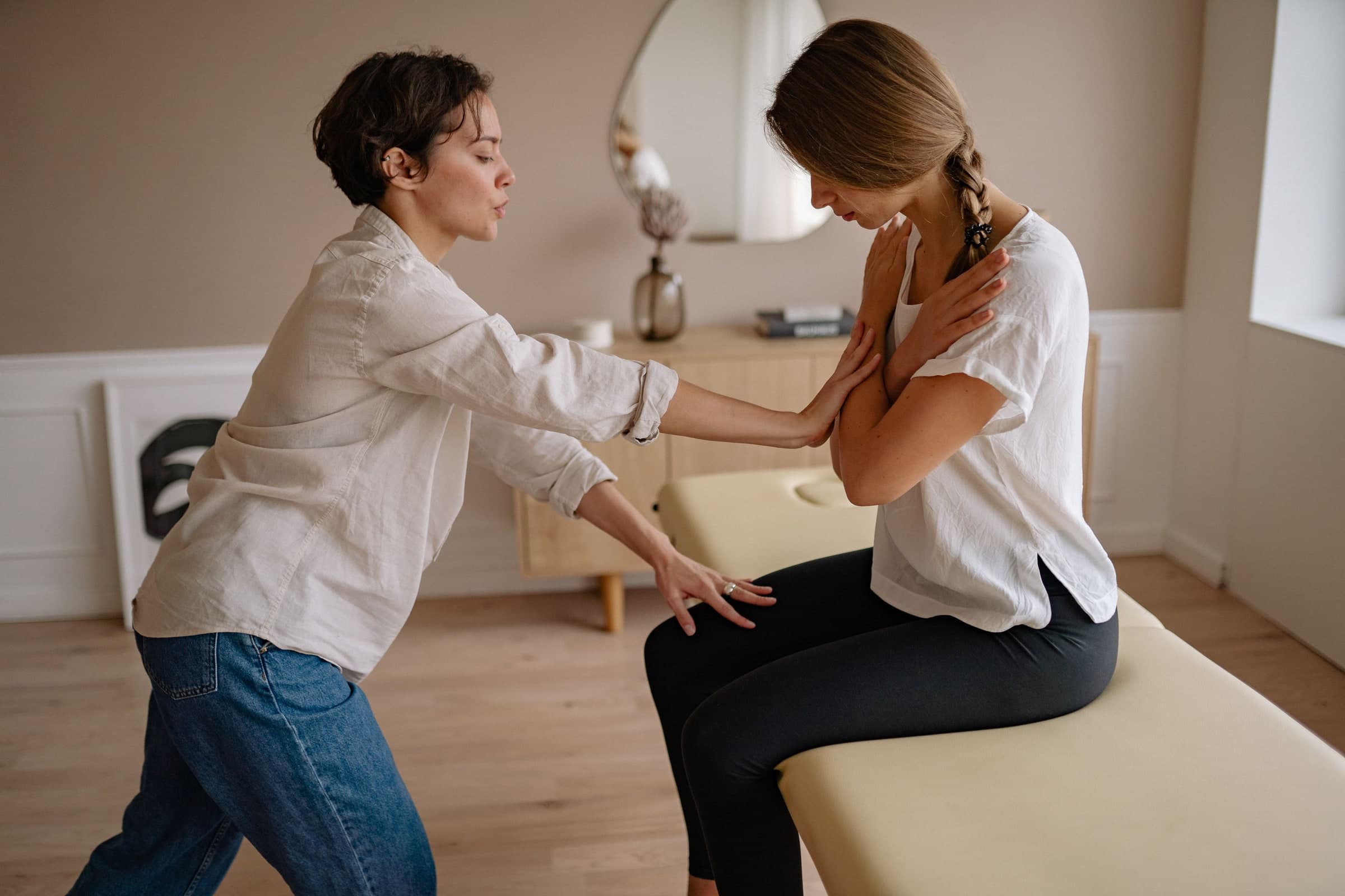 A healthcare practitioner performing a shoulder assessment on a patient seated on an examination table in a bright clinical room at a Toronto clinic