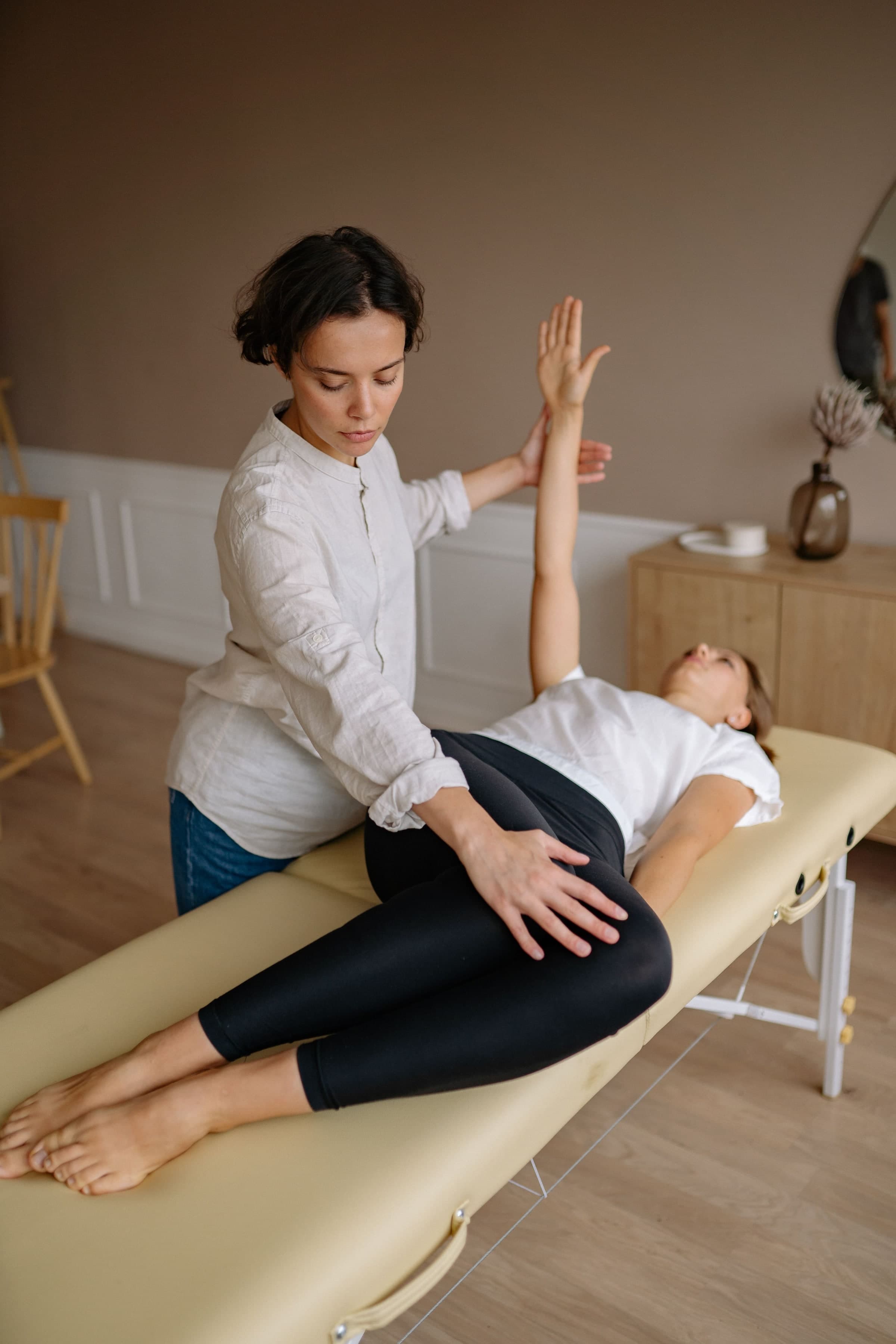 Physiotherapist performing a leg stretch on a patient lying on a treatment table in a bright clinic room, Toronto