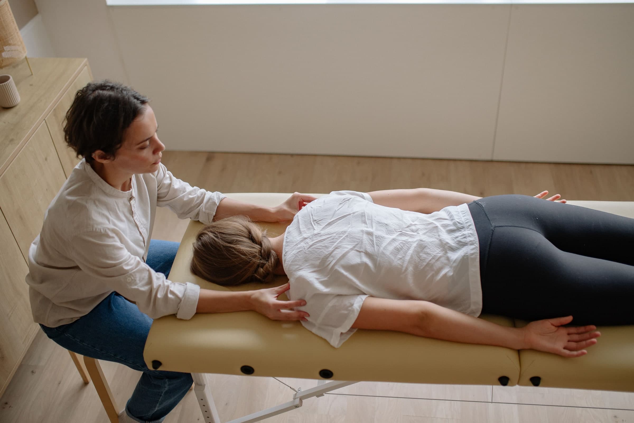 Physiotherapist performing manual therapy on a patient's lower back while the patient lies face-down on a treatment table in a clinical room in Toronto